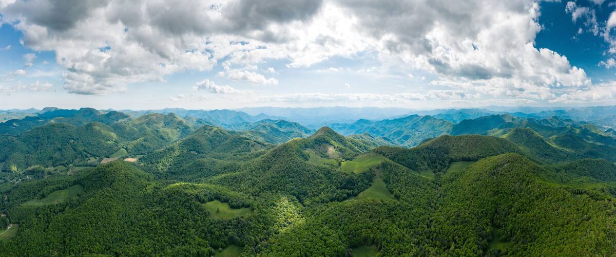 A mountainous landscape with dense forests and rolling hills under a partly cloudy sky.