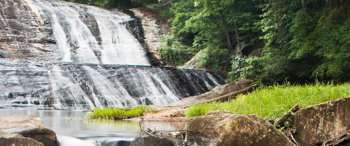A waterfall cascading over rocks into a stream surrounded by lush greenery.