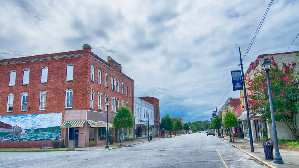 A quiet street lined with historic buildings, a mural on the left, and a clear sky.