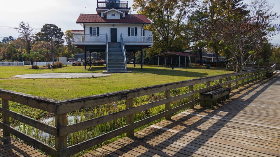 A white building with a red roof and a balcony, surrounded by a wooden deck and a grassy area.