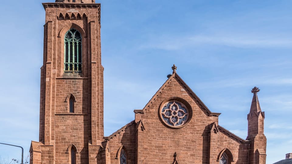 A brick church with a tall tower, a large circular stained glass window, and a red door.
