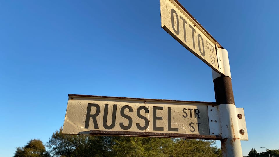 Street signs for 'OTTO ST' and 'RUSSEL STR' against a clear blue sky.