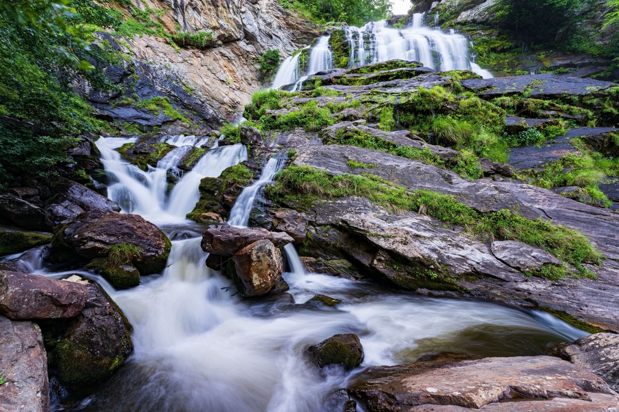 Una cascada en varios niveles que desciende sobre rocas cubiertas de musgo en un exuberante bosque verde.