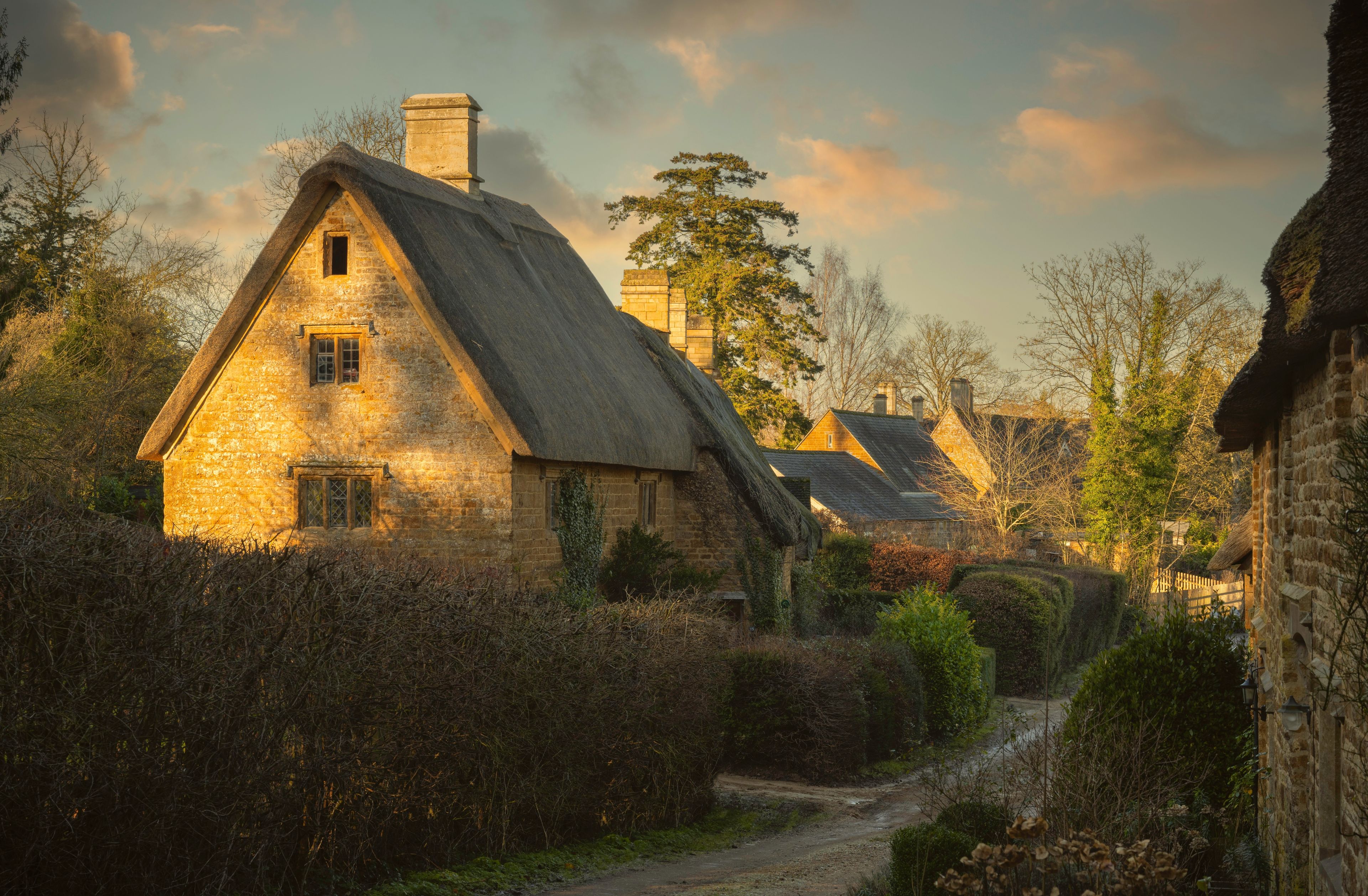A quaint village with stone houses, a narrow dirt path, and lush greenery.