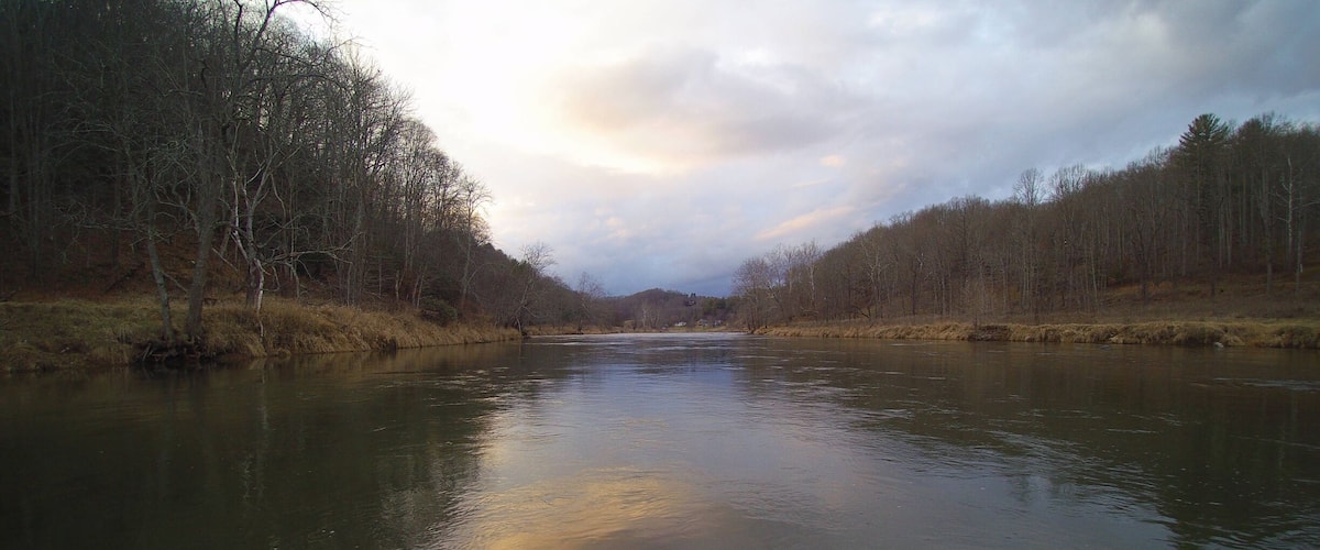 A river flanked by leafless trees under a cloudy sky.