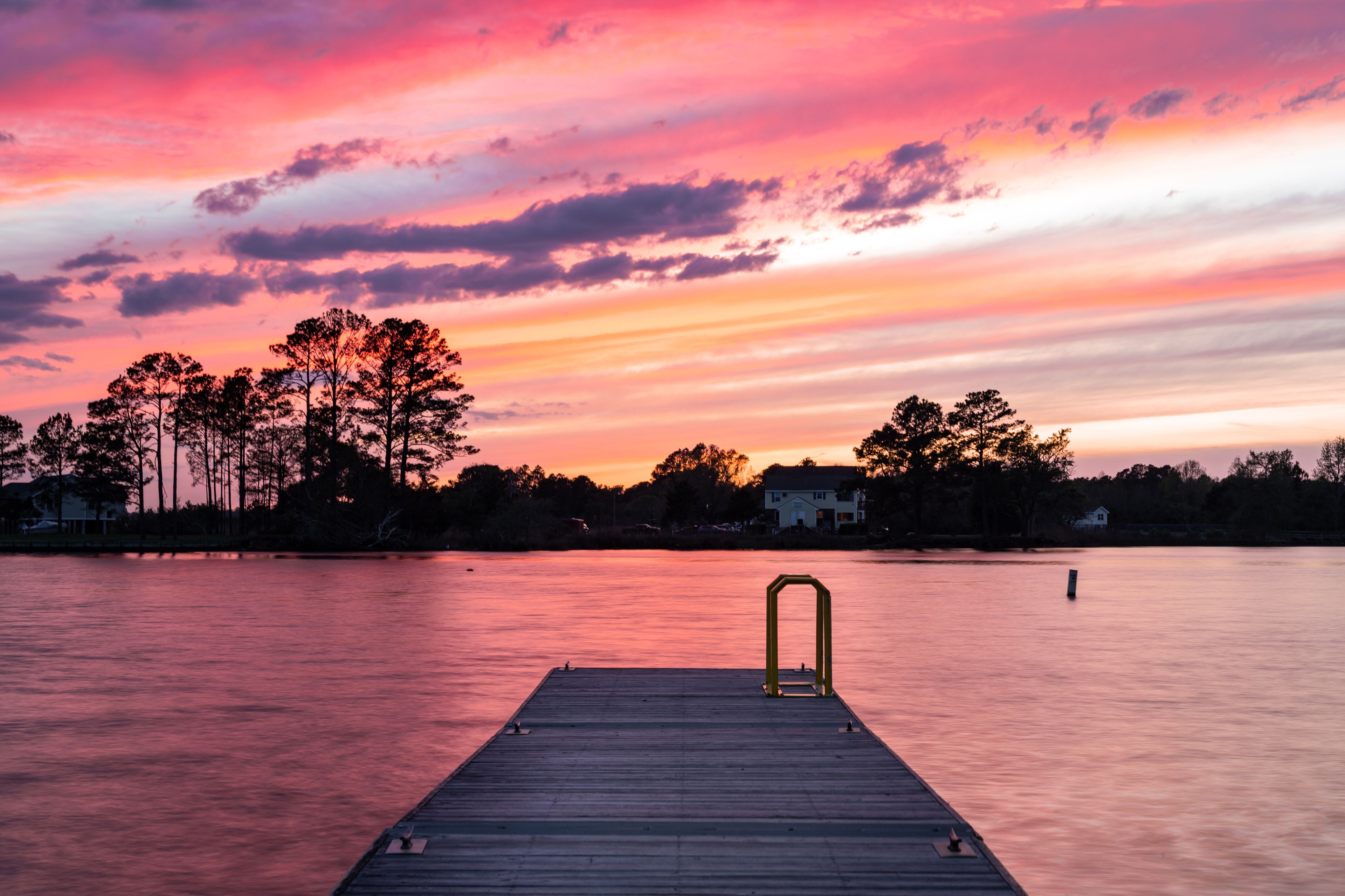 A wooden pier extending into a body of water with a sunset sky.