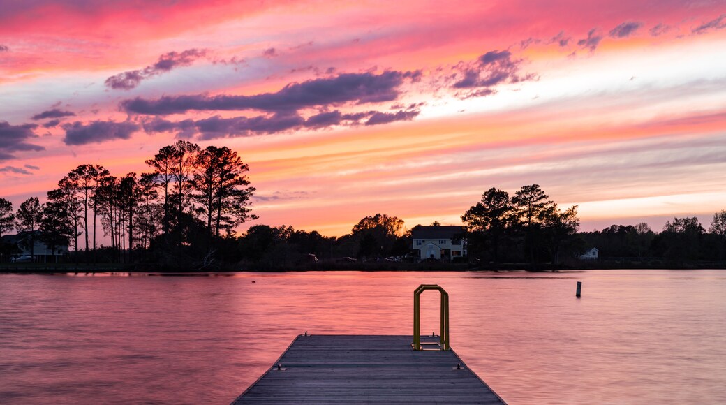 A wooden pier extending into a body of water with a sunset sky.