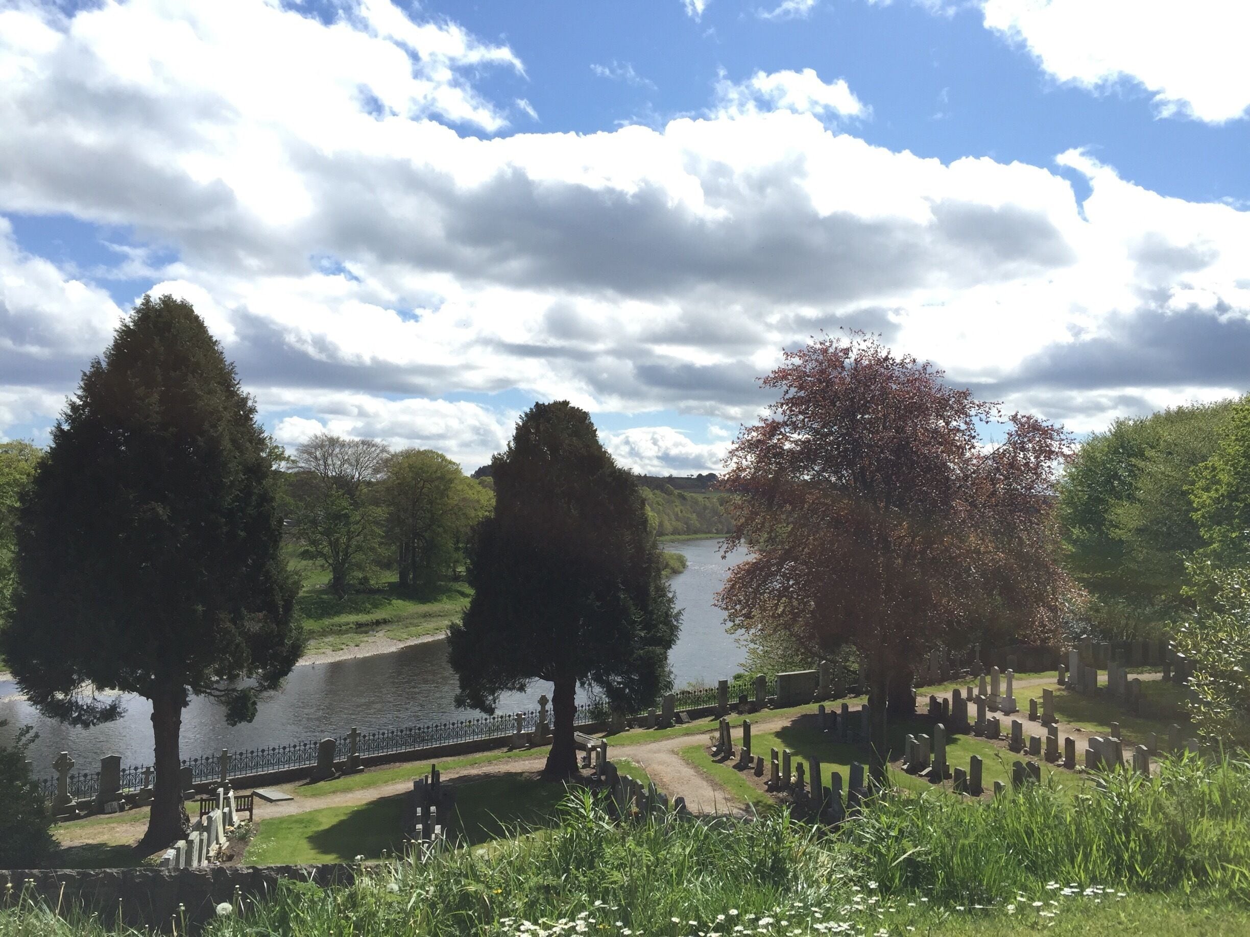 A cemetery with a lake, trees, and a cloudy sky.