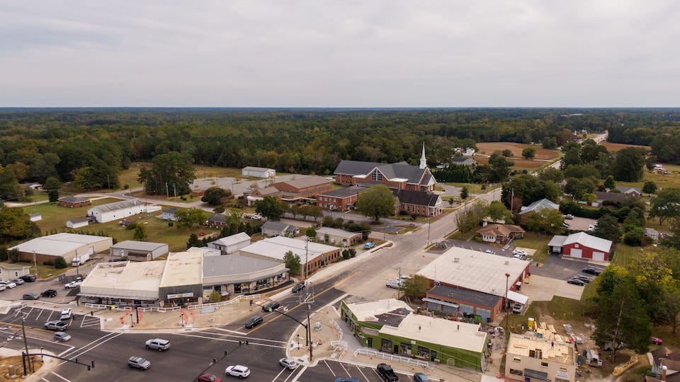 A town with a central intersection, surrounded by buildings, roads, and greenery.