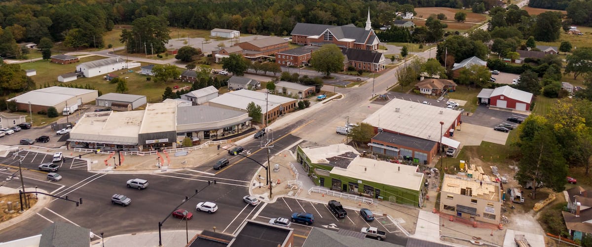 A town with a central intersection, surrounded by buildings, roads, and greenery.