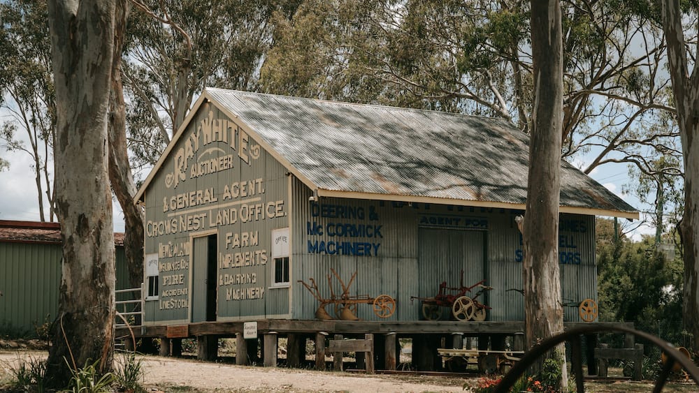 A rustic building with signs advertising various services like auctioneering, general agent, and farm implements.