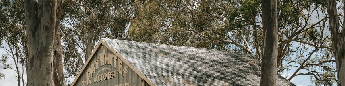 A rustic building with signs advertising various services like auctioneering, general agent, and farm implements.