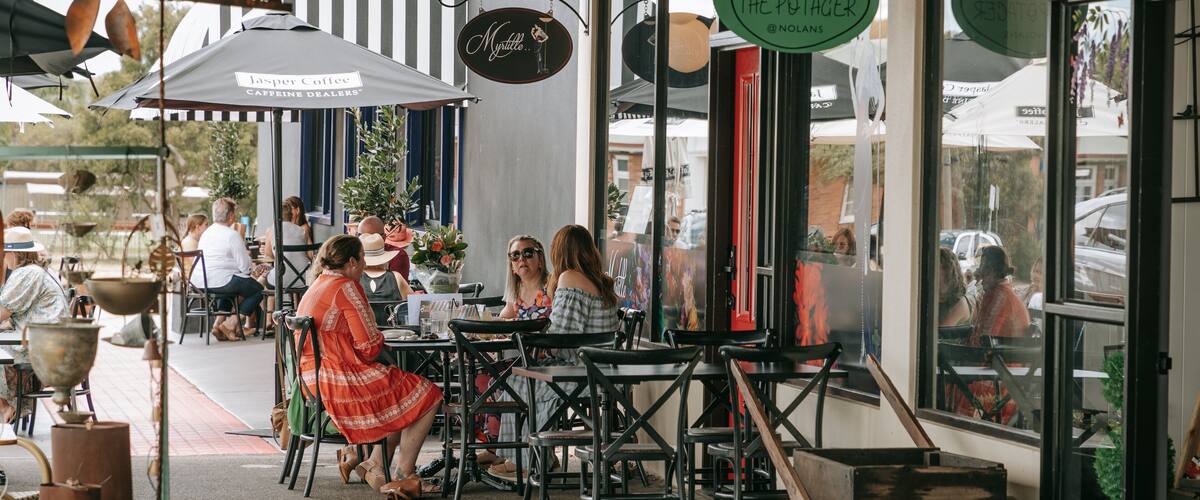An outdoor café with tables and chairs, a sign for Jasper Coffee Caffeine Dealers, and a sign for The Potager.