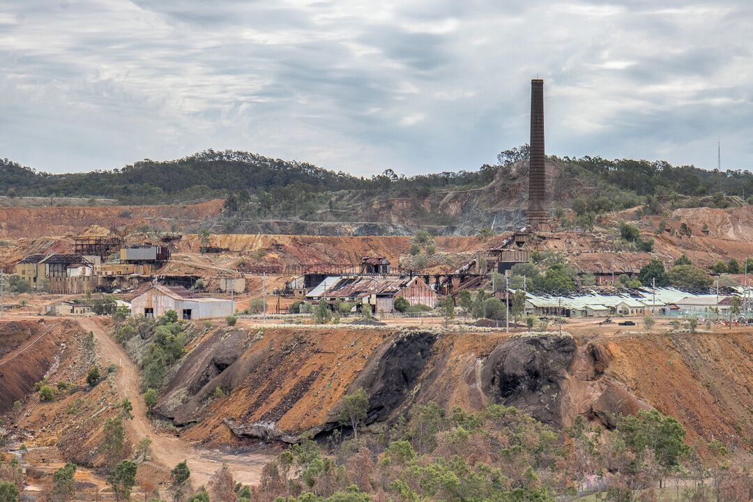 Uma área de mineração com uma chaminé alta, valas abertas e edifícios espalhados.