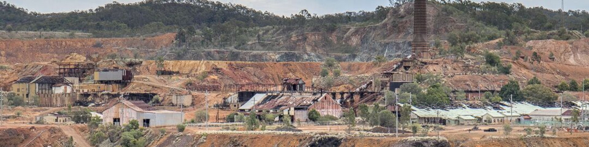 Uma área de mineração com uma chaminé alta, valas abertas e edifícios espalhados.