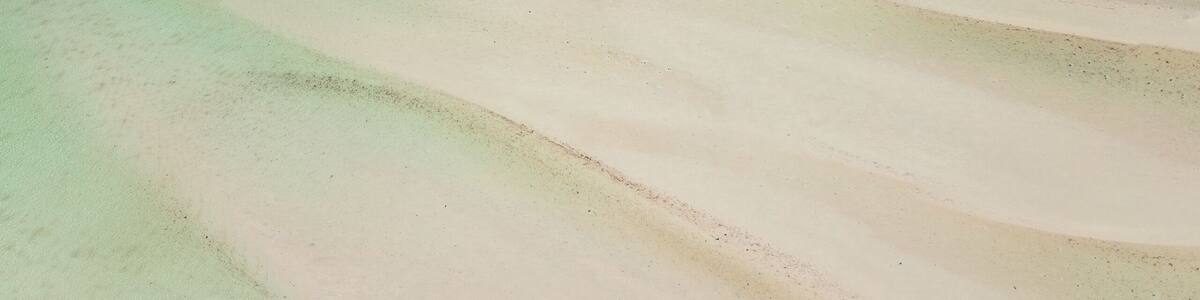 A vast sandy beach with clear blue waters and a distant shoreline.