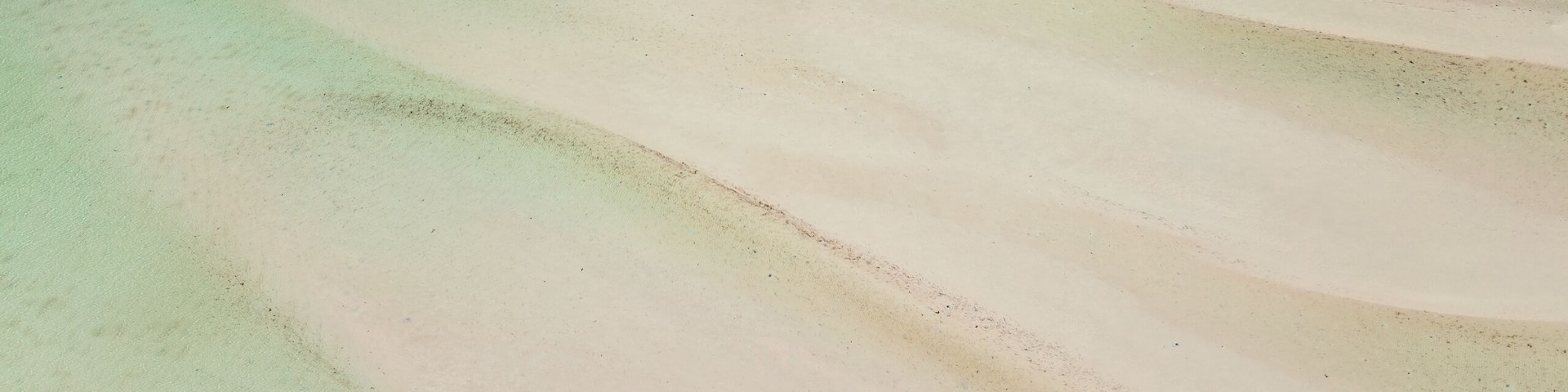 A vast sandy beach with clear blue waters and a distant shoreline.