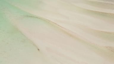 A vast sandy beach with clear blue waters and a distant shoreline.
