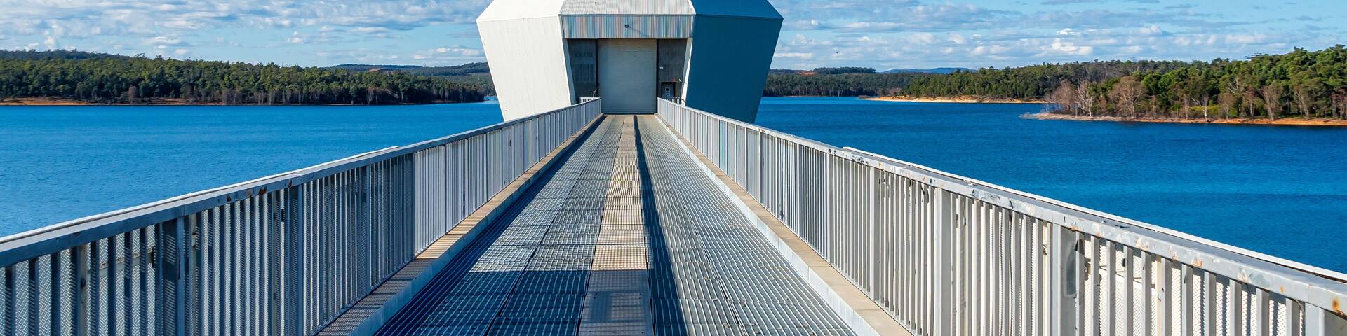 A bridge with a metal walkway leading to a white building with a large garage door.