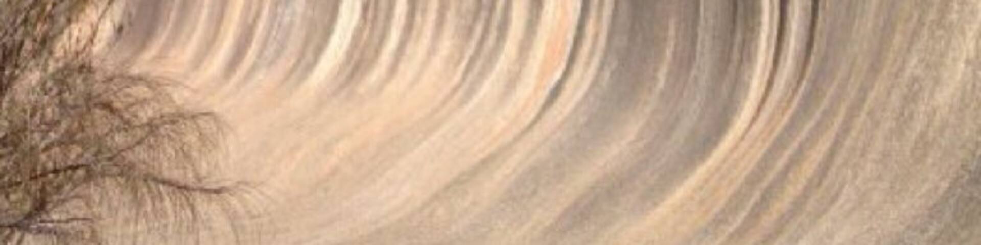 A large, smooth, wave-like rock formation with a clear sky above.
