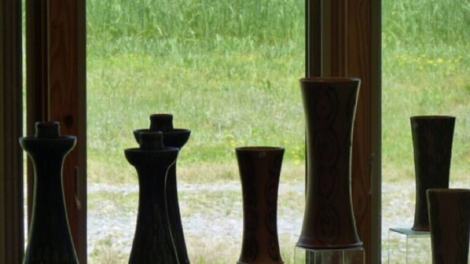 A display of vases by a window overlooking a grassy field.