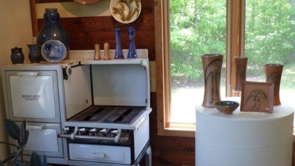 A rustic kitchen with wooden walls, a vintage stove, and various pottery items displayed on a shelf.