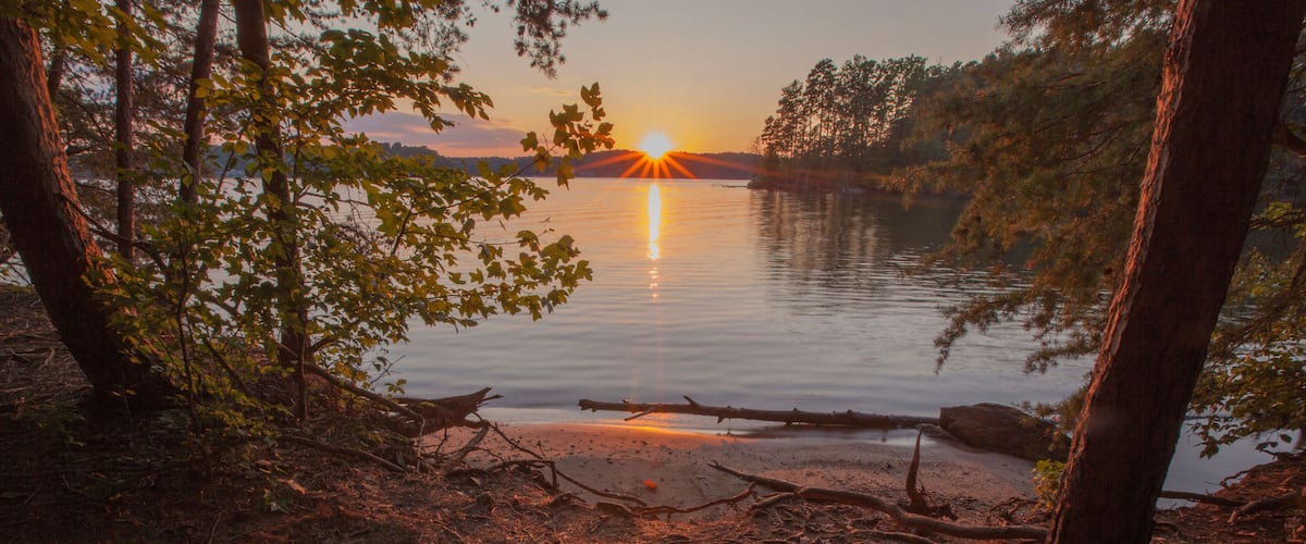 A sunset over a calm lake surrounded by trees.