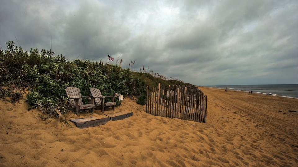 A sandy beach with wooden chairs and a wooden fence.