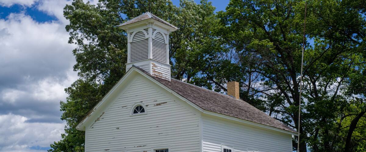 A white church with a steeple and a sign that reads "Spencer Brook School".