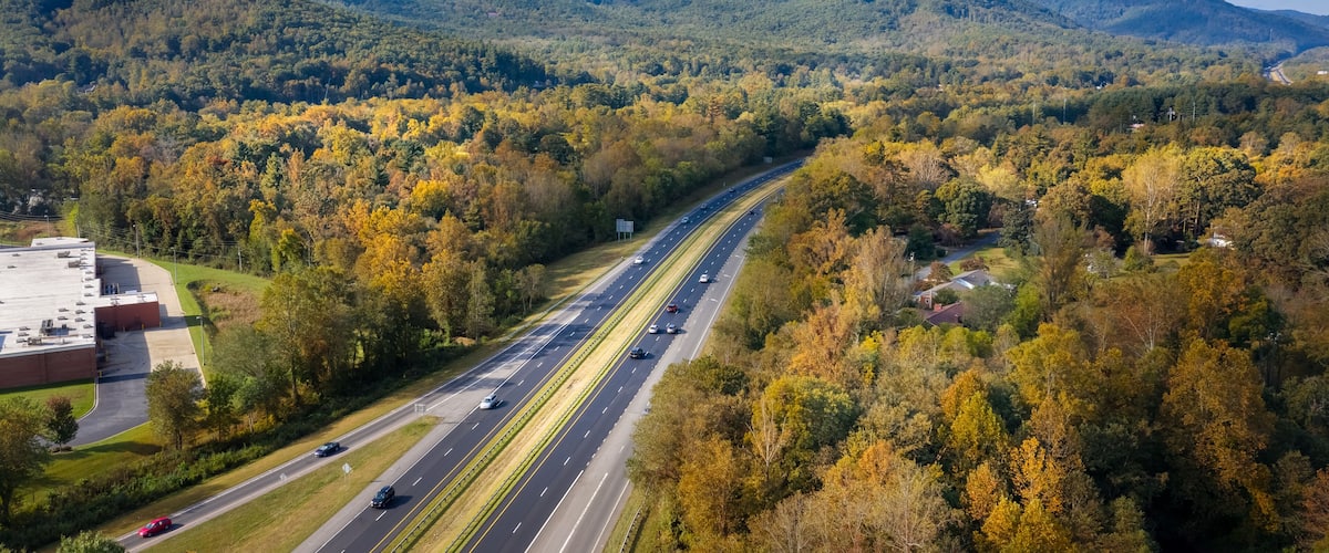 A highway surrounded by autumn-colored trees and mountains.