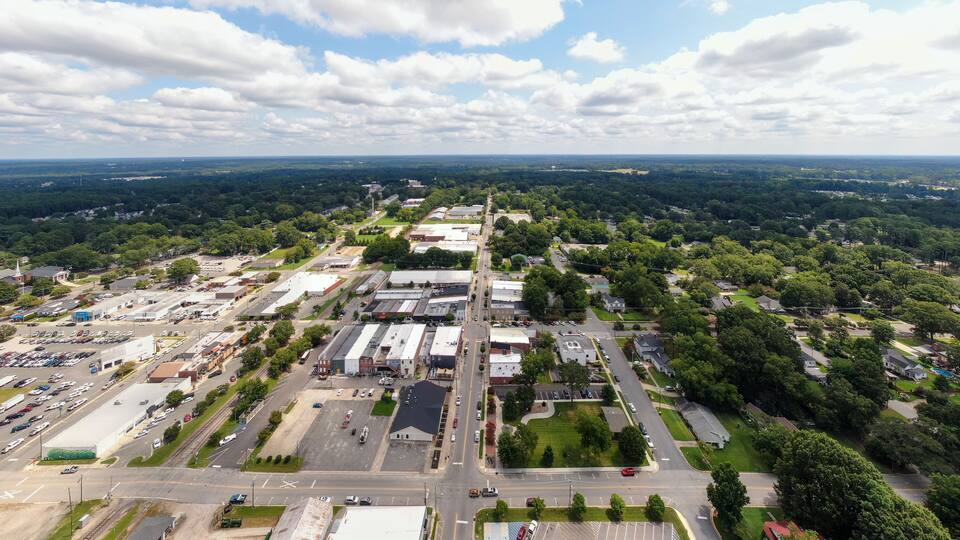 An aerial view of a town with industrial buildings, parking lots, and surrounding greenery.