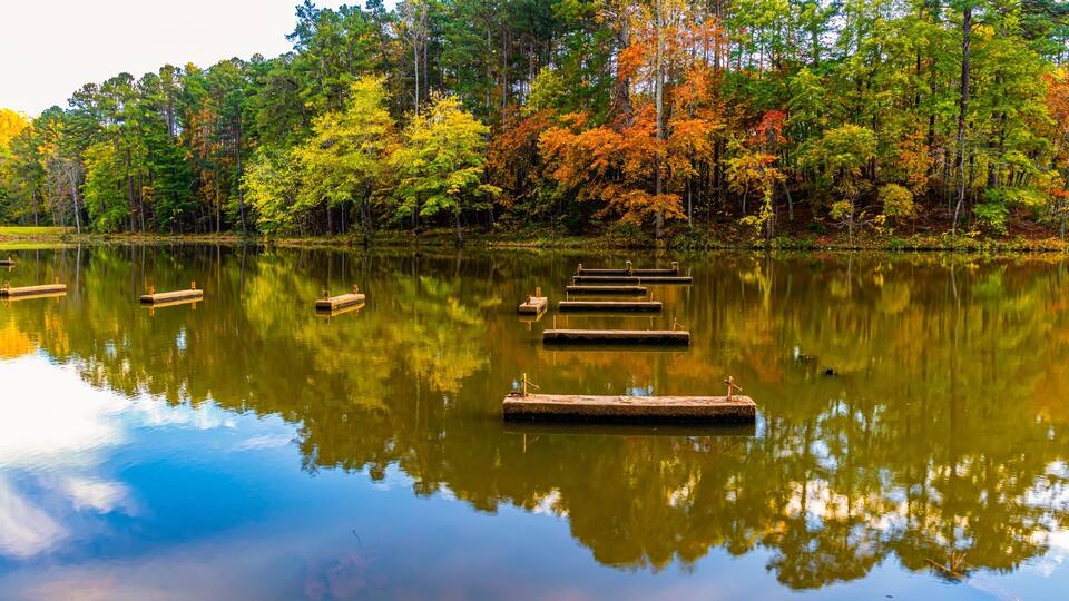 A calm lake with wooden docks and autumn-colored trees reflecting on the water.