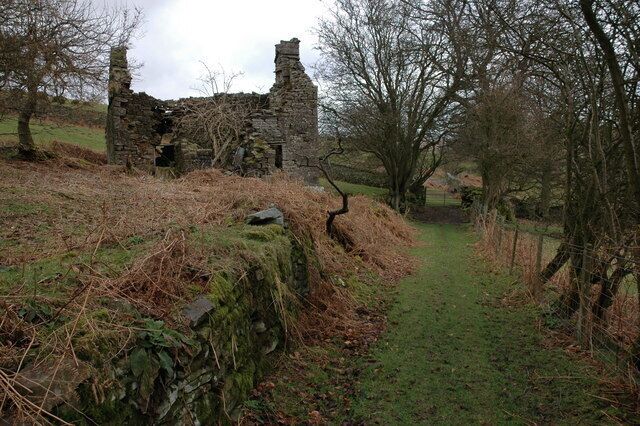 A stone ruin with overgrown vegetation and a narrow path leading through it.