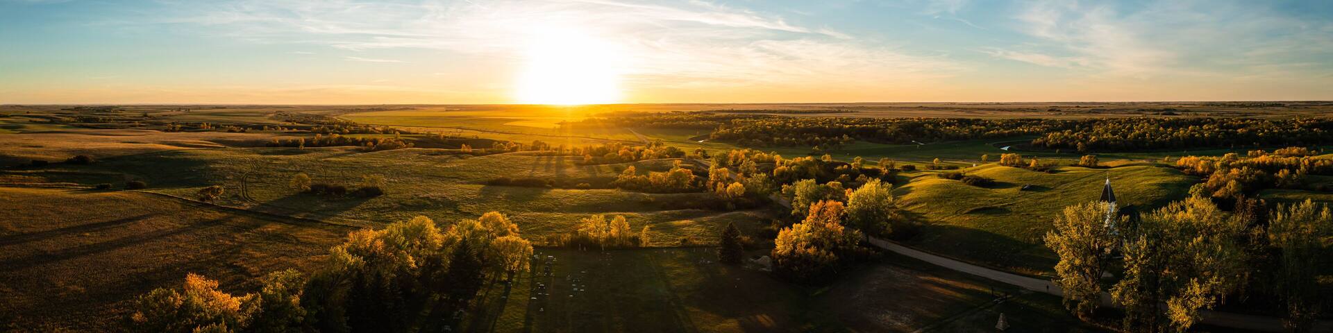 Aerial panorama of a sunset over the gentle rolling hills of the Great Plains with trees in their autumn colors in North Dakota.