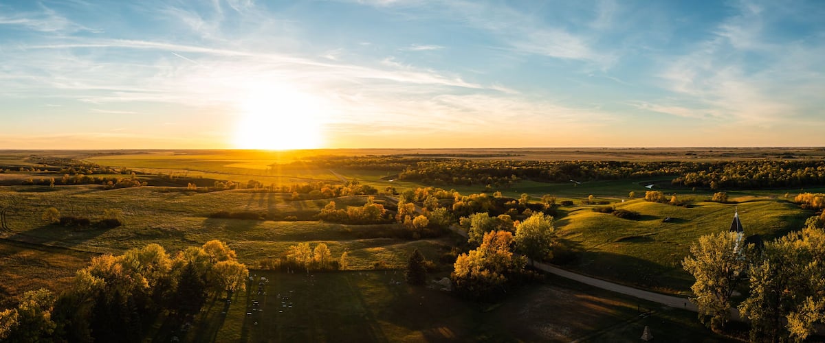 A sunset over rolling hills with a road and trees.