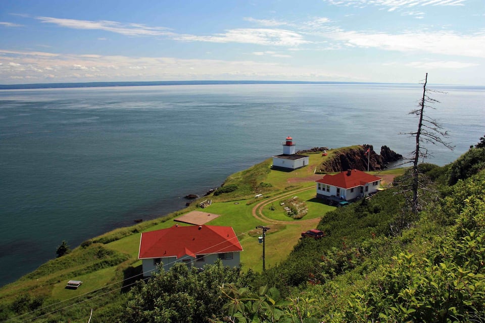 Paesaggio costiero con un faro, zone erbose e vista libera sul mare.