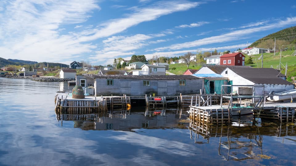 A calm waterfront with docked boats, a red house, and a small white building.