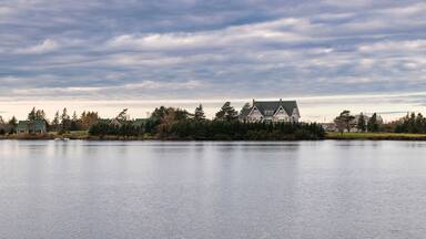 A large house by a calm lake with a cloudy sky.