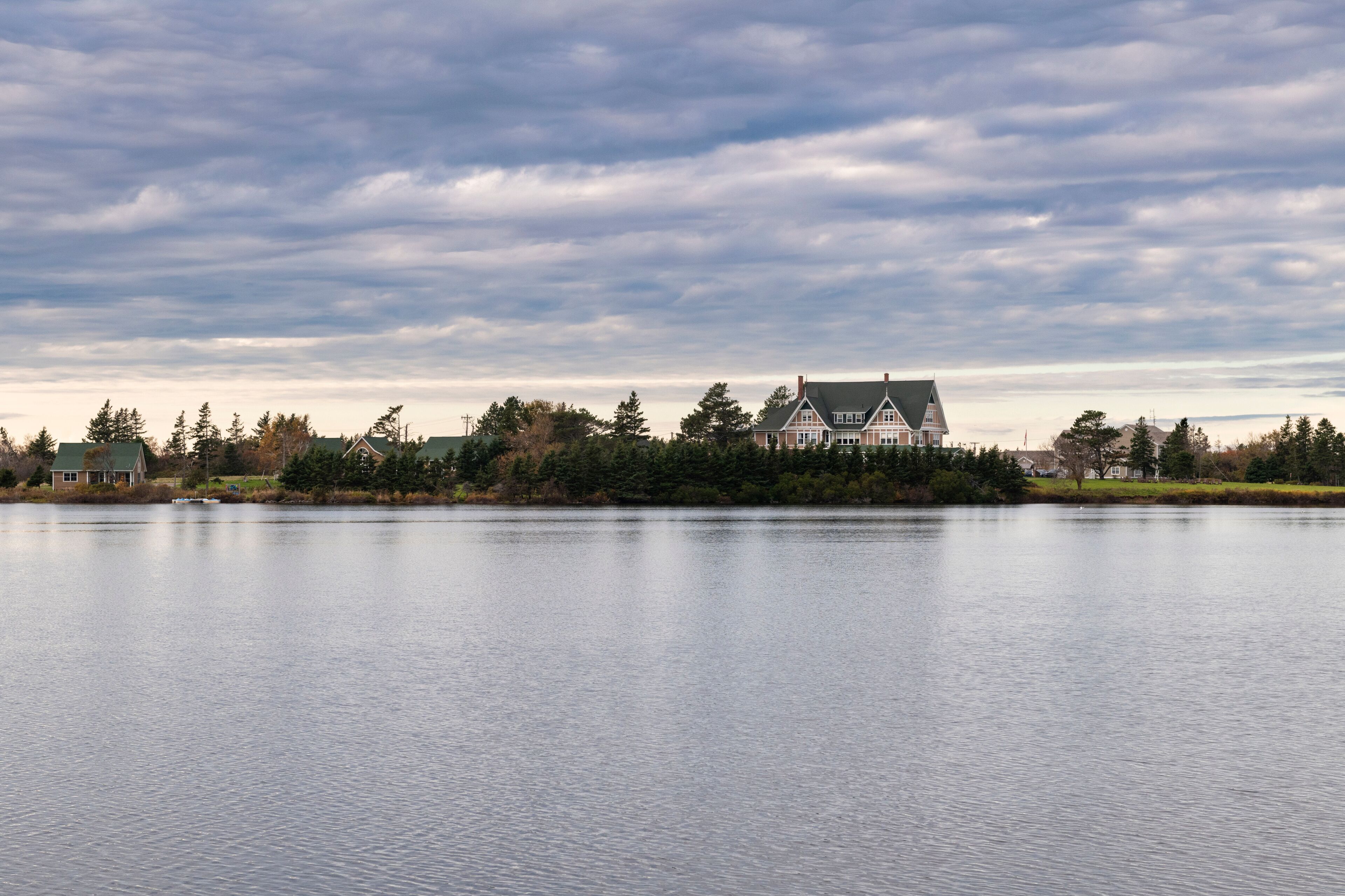 A large house by a calm lake with a cloudy sky.