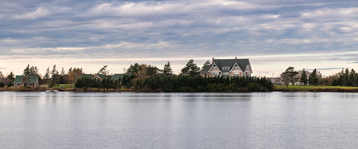 A large house by a calm lake with a cloudy sky.