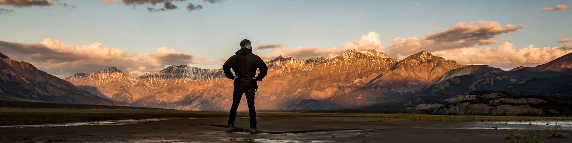 Une personne se tient sur une surface d’eau qui reflète l’image, avec des montagnes en arrière-plan.