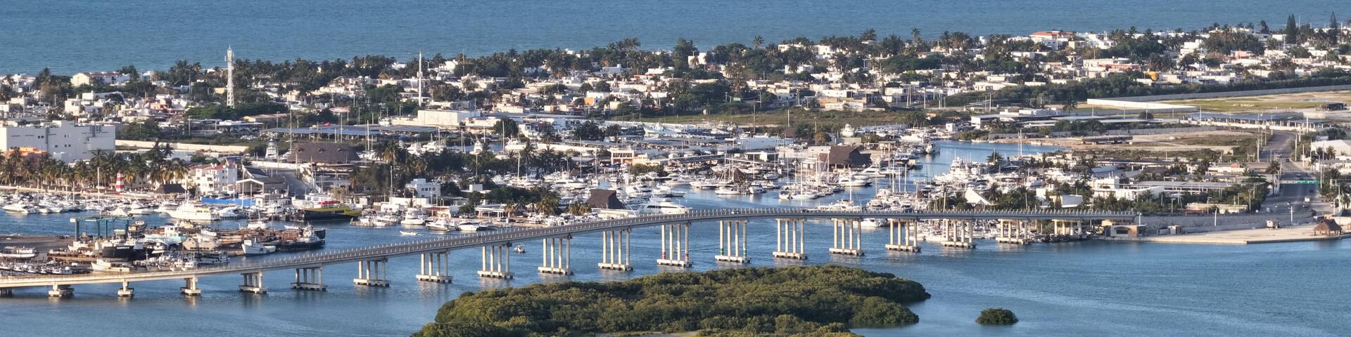 A coastal city with a marina, a bridge, and a small island with dense vegetation.