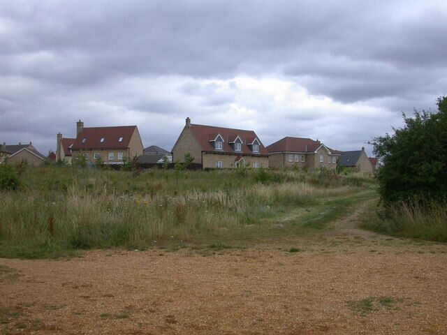 A rural landscape with houses, a gravel path, and overcast skies.
