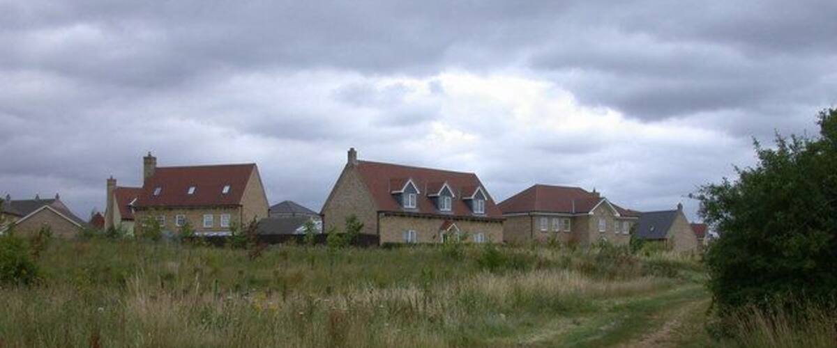 A rural landscape with houses, a gravel path, and overcast skies.