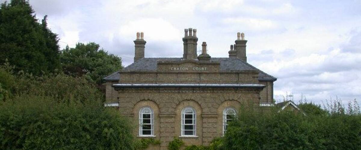 A stone building labeled "CAXON COURT" with a gravel driveway and dense greenery around.