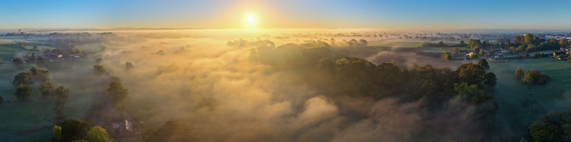 A sunrise over a misty landscape with scattered houses and trees.