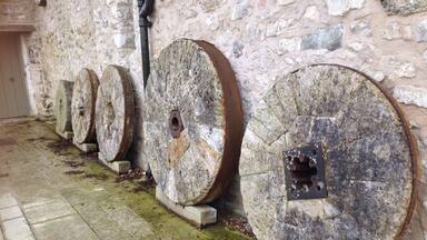 Heron Corn Mill
Beetham
Milnthorpe
Lancs
Water-powered corn mill, with attached grain dryer and water supply mechanism and launder. Late C18 or earlier, remodelled and enlarged C19, restored as a museum in 1975. Rubble stone, slobbered, with a slate roof laid to diminishing courses. PLAN: L-shaped complex with main mill range aligned parallel to the River Bela, and ancillary range at right angles to the north-west. EXTERIOR: River frontage to south-east with dressed stone plinth and semi circular arch-headed double doorway to lower level. 3 multi-pane upper floor windows with flat-arched heads. Wide south-east gable with timber launder leading from sluice gates with rack and pinion mechanisms. Narrow extension to north-west incorporates corn drying kiln with roof louvre. Single bay north-east elevation with a C20 window frame to each floor and a board door. INTERIOR: The restoration of the mill interior was completed in 1975, and contains a Lowder stone frame on the stone floor and complete associated machinery, driven by a 14ft overshot water wheel. Line shafting in the attic powers the sack hoist which raises grain to the highest part of the building, to be delivered by gravity onto the 4 pairs of millstones below. The roof structure is supported on trusses with curved knee braces to the principles. HISTORY: The mill site is thought to have had medieval origins, rights to erect and run a corn mill having been granted to the Canons of Coningshead in 1220. The present mill operated until 1955. A water-powered corn mill on a mill site established in 1220 and operated until 1955, with a complete and working interior, including a rare survival of a Lowder frame.
