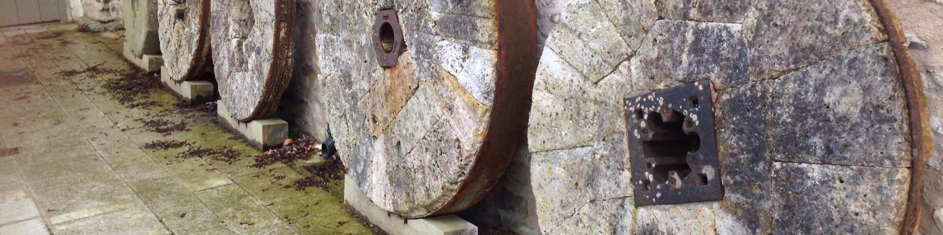 Heron Corn Mill
Beetham
Milnthorpe
Lancs
Water-powered corn mill, with attached grain dryer and water supply mechanism and launder. Late C18 or earlier, remodelled and enlarged C19, restored as a museum in 1975. Rubble stone, slobbered, with a slate roof laid to diminishing courses. PLAN: L-shaped complex with main mill range aligned parallel to the River Bela, and ancillary range at right angles to the north-west. EXTERIOR: River frontage to south-east with dressed stone plinth and semi circular arch-headed double doorway to lower level. 3 multi-pane upper floor windows with flat-arched heads. Wide south-east gable with timber launder leading from sluice gates with rack and pinion mechanisms. Narrow extension to north-west incorporates corn drying kiln with roof louvre. Single bay north-east elevation with a C20 window frame to each floor and a board door. INTERIOR: The restoration of the mill interior was completed in 1975, and contains a Lowder stone frame on the stone floor and complete associated machinery, driven by a 14ft overshot water wheel. Line shafting in the attic powers the sack hoist which raises grain to the highest part of the building, to be delivered by gravity onto the 4 pairs of millstones below. The roof structure is supported on trusses with curved knee braces to the principles. HISTORY: The mill site is thought to have had medieval origins, rights to erect and run a corn mill having been granted to the Canons of Coningshead in 1220. The present mill operated until 1955. A water-powered corn mill on a mill site established in 1220 and operated until 1955, with a complete and working interior, including a rare survival of a Lowder frame.