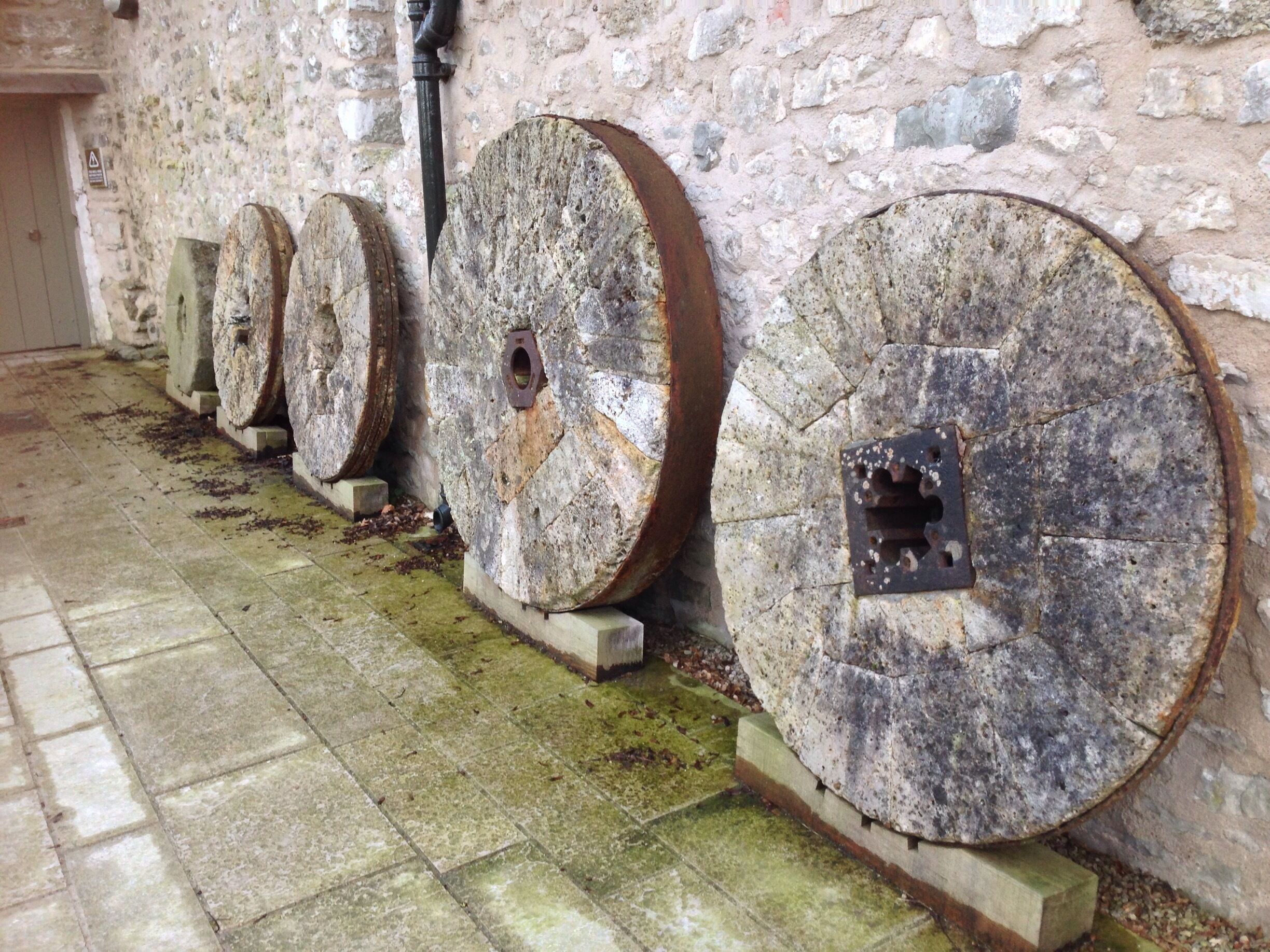 A row of large, weathered stone wheels mounted on a wall, with moss and dirt accumulation.