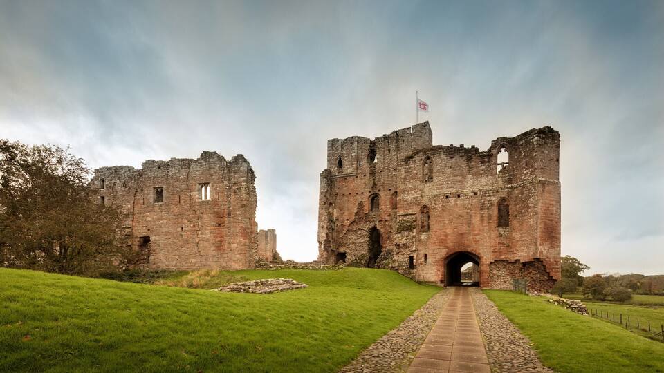 A historic castle with a flag, ruins, and a grassy pathway.